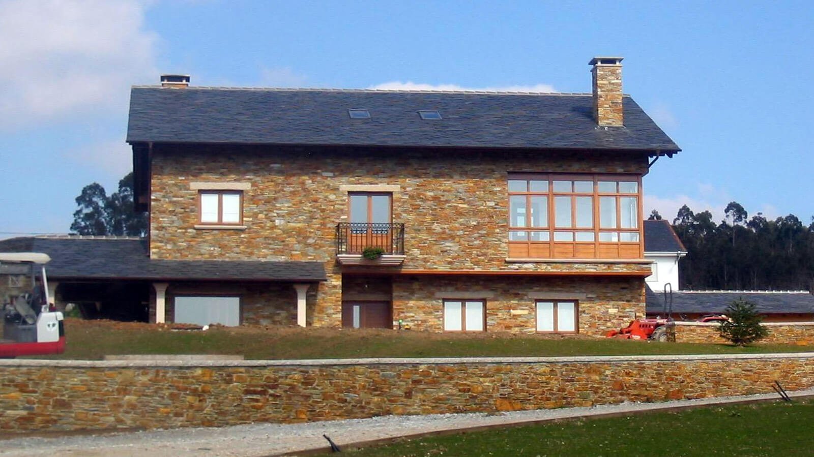 Casa con fachada y muro de jardín revestidos de piedra cuarcita natural y tejado de pizarra