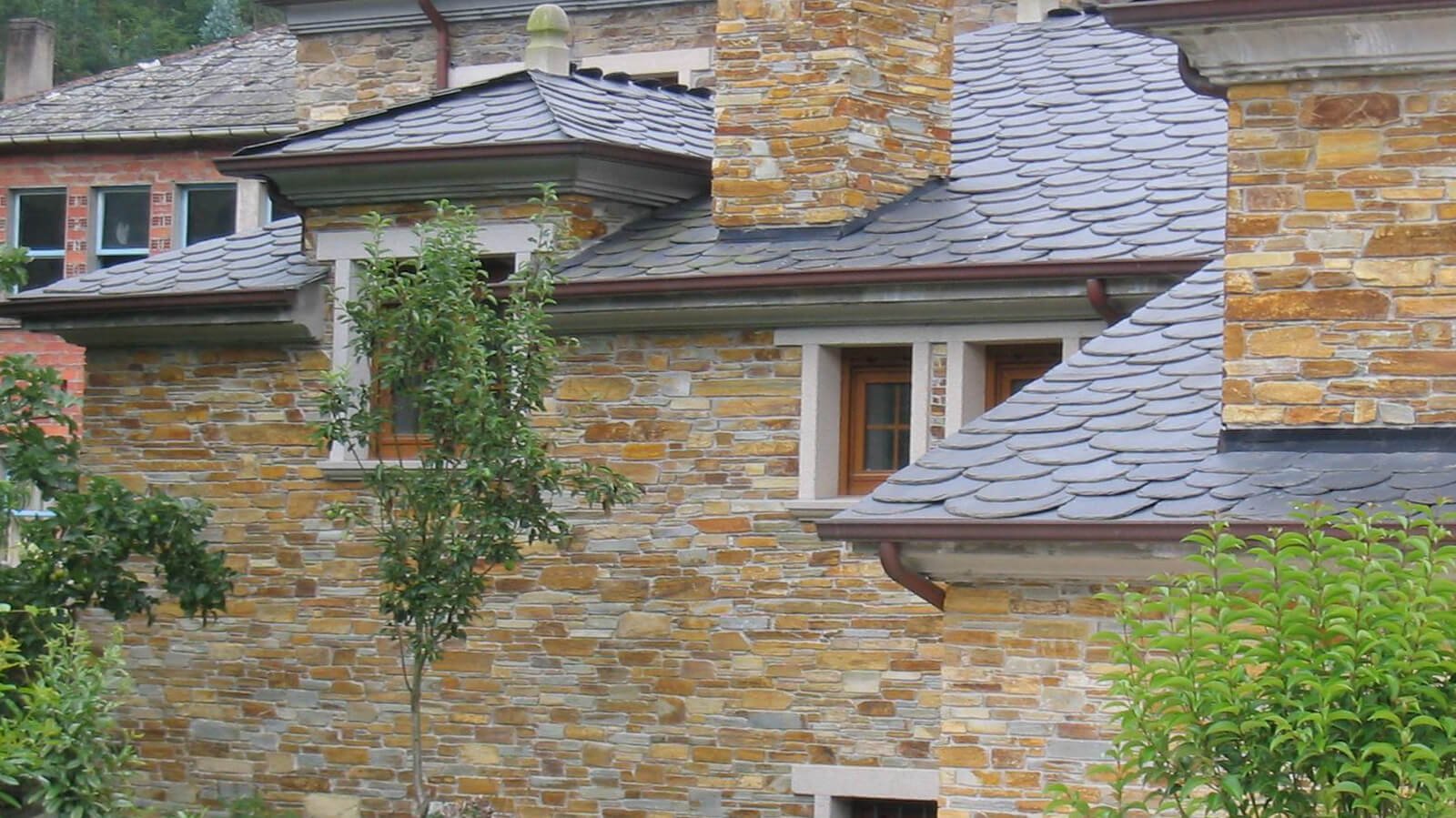 Fachada de vivienda revestida con laja de cuarcita y tejado de pizarra